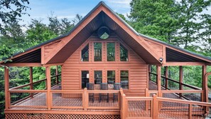 A wooden cabin with a balcony, large windows, and a chimney.