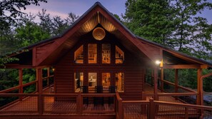 A log cabin with a wrap-around porch, multiple windows, and a staircase leading to the entrance.