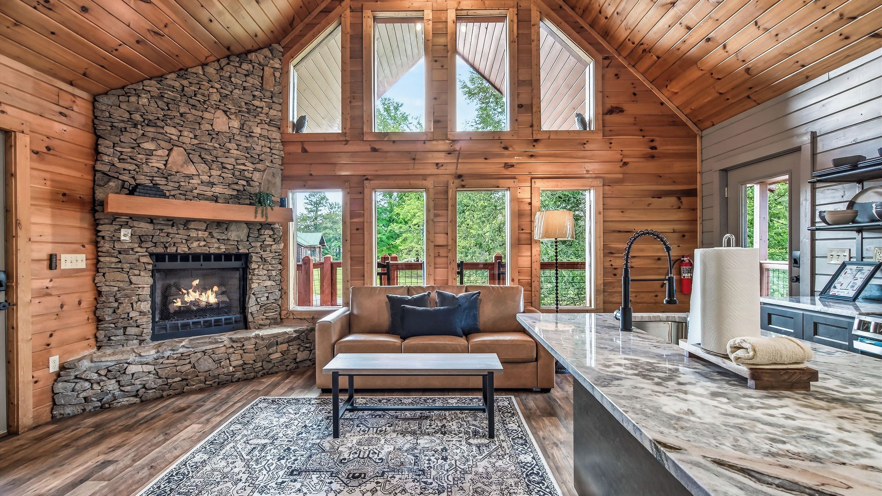 A log cabin interior with a stone fireplace, a sofa, a coffee table, and a kitchen area with a marble countertop.