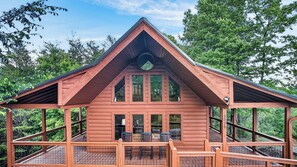 A cabin with a gabled roof, large windows, and a deck with chairs.
