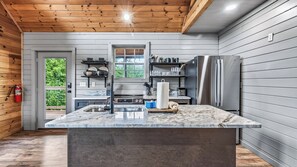 A modern kitchen with a marble countertop, stainless steel appliances, and a wooden ceiling.