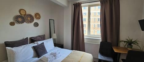 A hotel room with a bed, a desk, a chair, a window with curtains, and wall decorations.