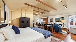 A bedroom with a large bed, wooden wardrobe, and a dining area with chairs and a table.