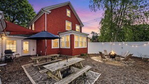 Ein rotes Haus mit einer Terrasse, auf der Picknicktische und eine Feuerstelle stehen.