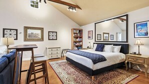 Ein Schlafzimmer mit einem Bett, Nachttischen, einem Schreibtisch, einem Sessel, einem Bücherregal und einem großen Spiegel.