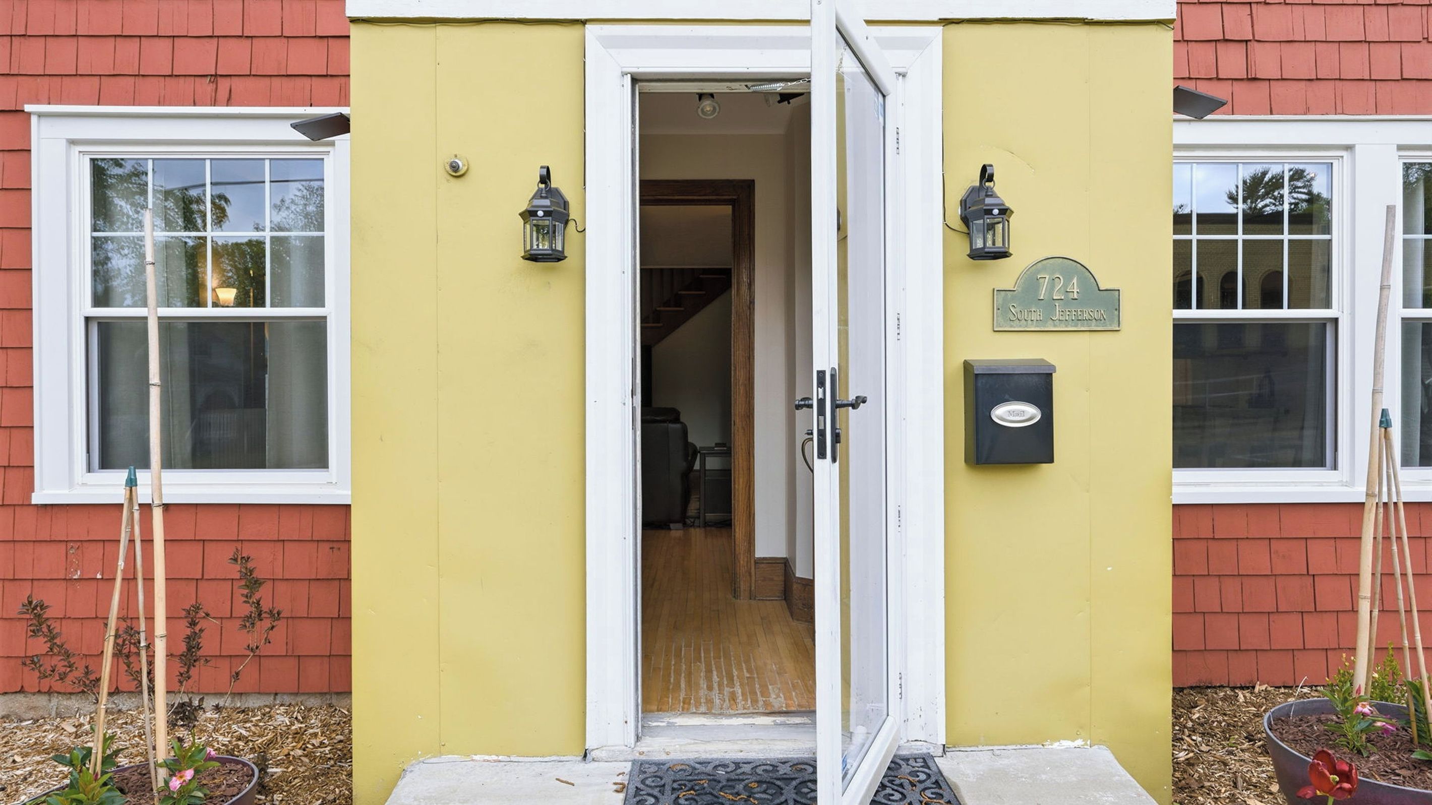 A yellow building with a white door, two windows, and a mailbox.