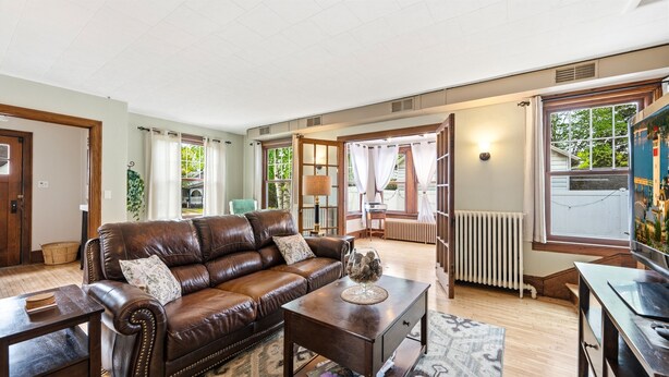 A spacious living room with a leather sofa, a coffee table, and a view of the outdoors through large windows. - Walk to Downtown Sturgeon Bay! Large Home + Yard (Sturgeon Bay)