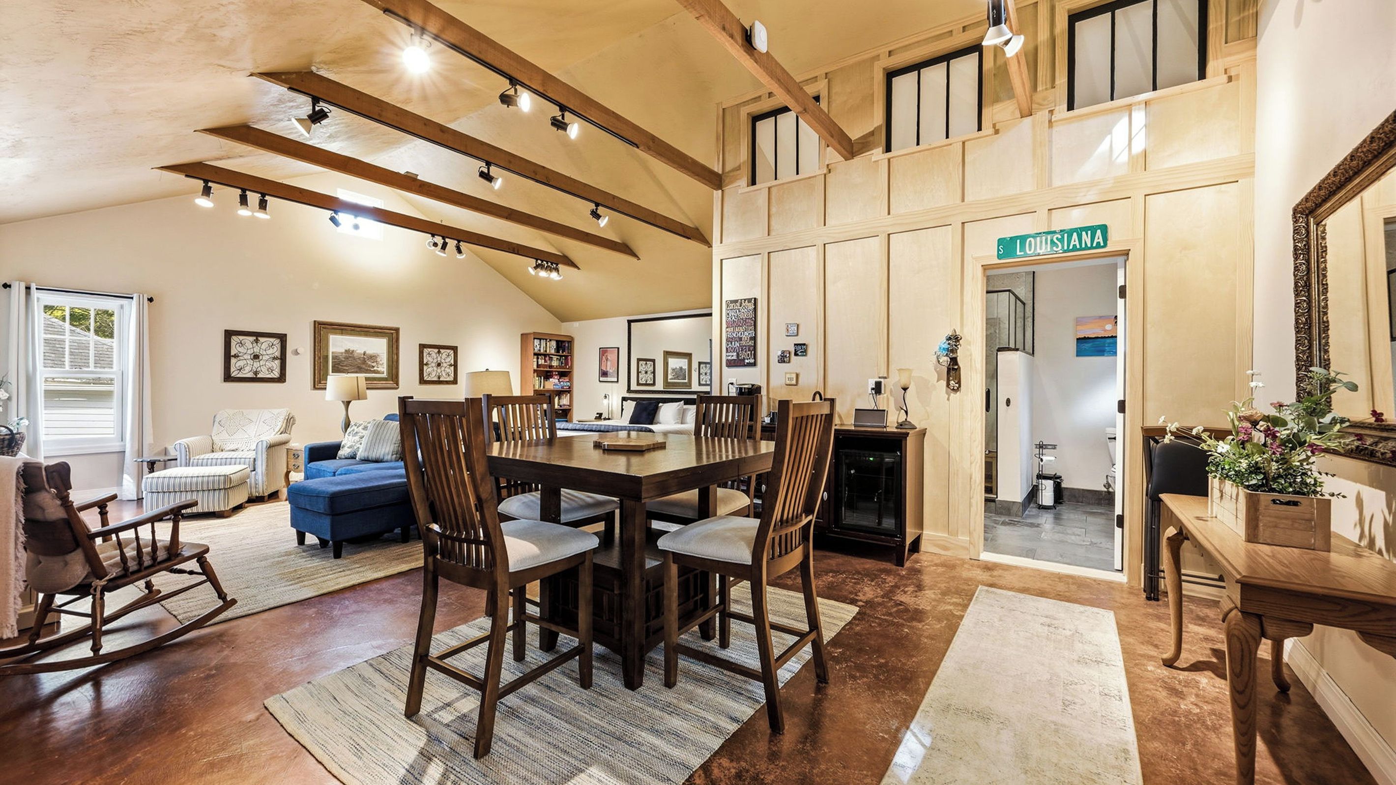 A spacious living room with a high ceiling, wooden beams, a dining area, and a view of the outside.