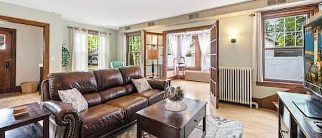 A living room with a brown leather sofa, a wooden coffee table, and a view of the outdoors through large windows.