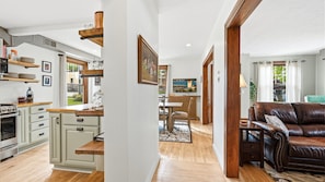 A spacious living area with a brown leather sofa, wooden flooring, and a view of the outdoors through a large window.