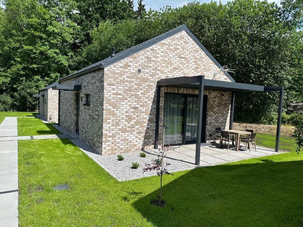 A modern building with a brick exterior, a covered patio area with outdoor furniture, and a small garden.