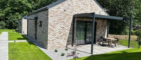 A modern building with a brick exterior, a covered patio area with outdoor furniture, and a small garden.