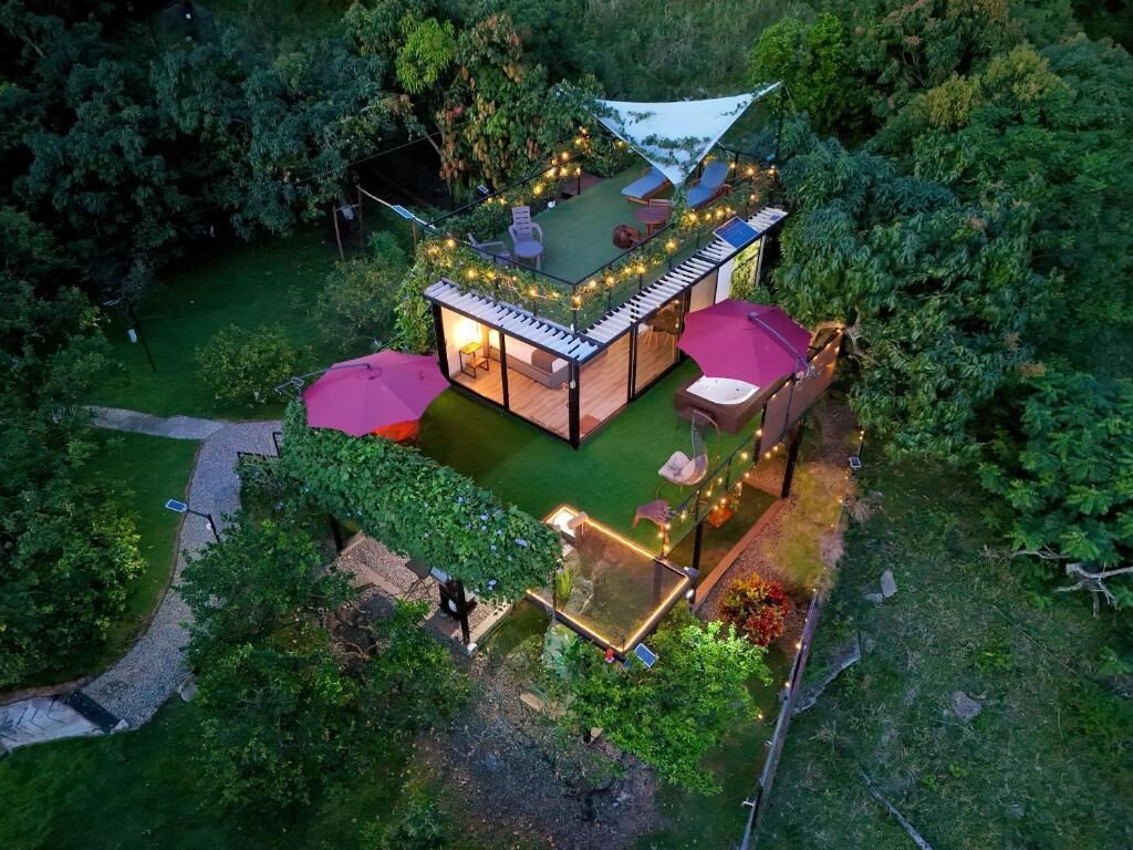 Una casa en el árbol con terraza, rodeada de vegetación, y equipada con mobiliario e iluminación exteriores.