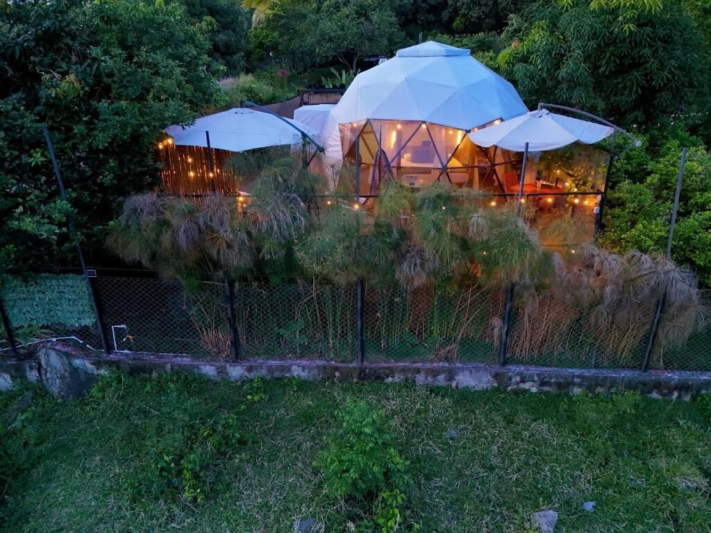 Un edificio de forma abovedada con varias habitaciones, rodeado de abundante vegetación y una cerca.
