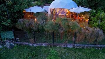 Un edificio de forma abovedada con varias habitaciones, rodeado de abundante vegetación y una cerca.
