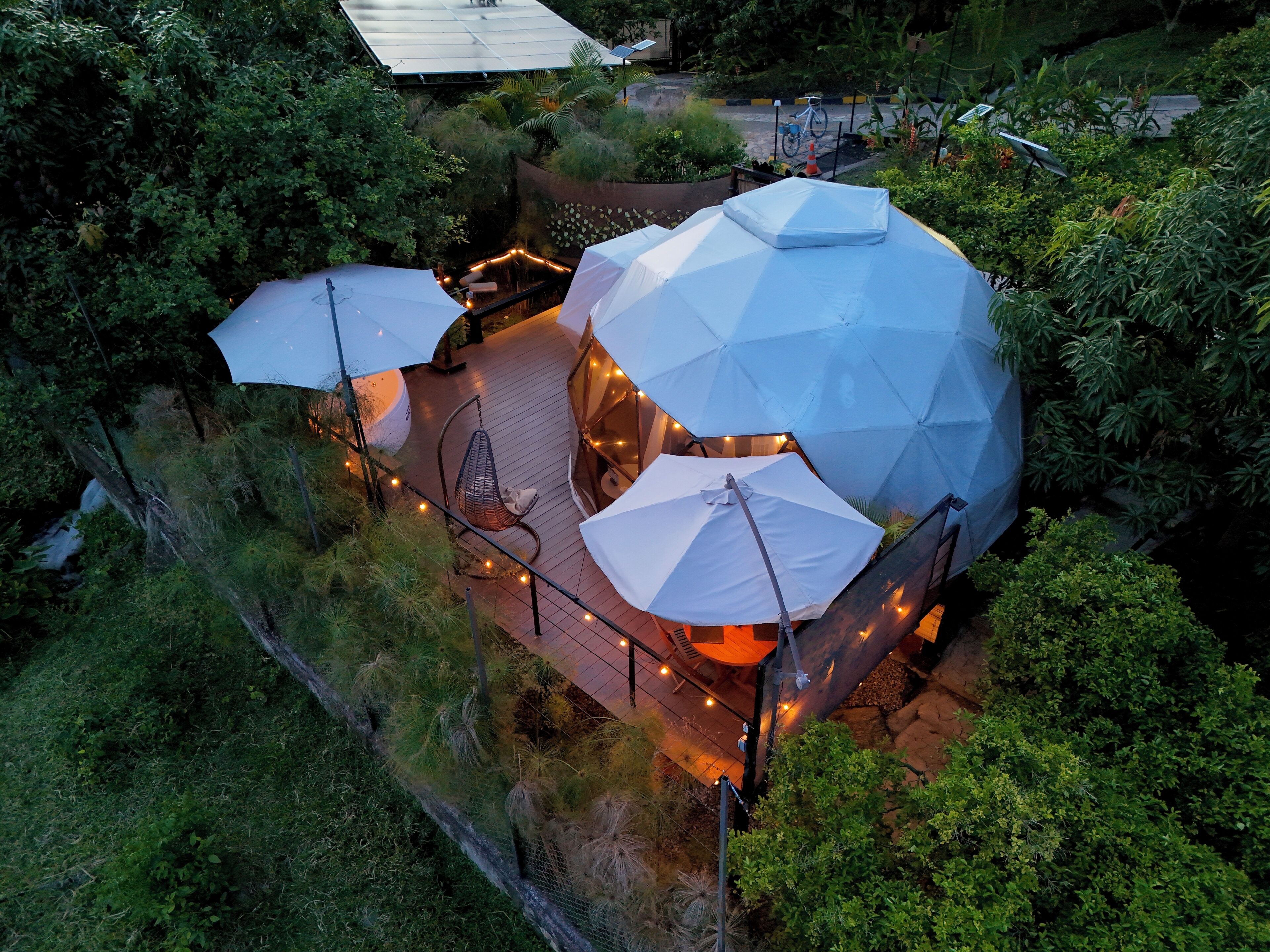 A geodesic dome structure with a patio area, surrounded by lush greenery.