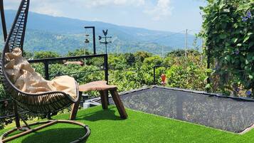 A rooftop terrace with artificial grass, a hanging chair, and a view of distant mountains.