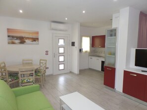 Eine moderne Wohnung mit Essbereich, einem Wohnzimmer mit grünem Sofa, einer Küche mit roten Schränken und einem Fernseher auf einem Lowboard.