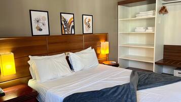 Quarto de hotel com cama, abajures, mesa de cabeceira, guarda-roupa e três quadros na parede.