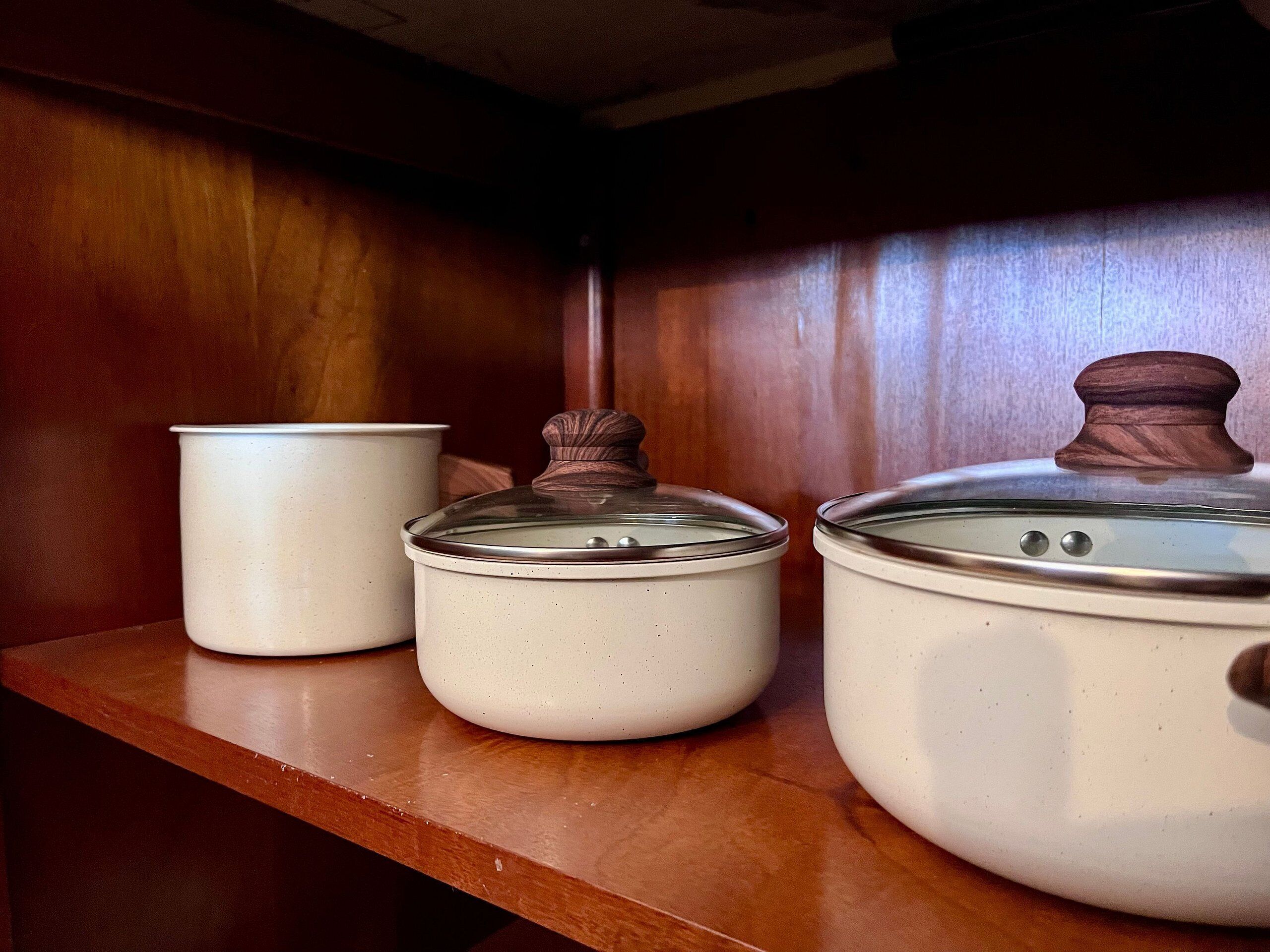 Three white ceramic containers with lids on a wooden shelf.