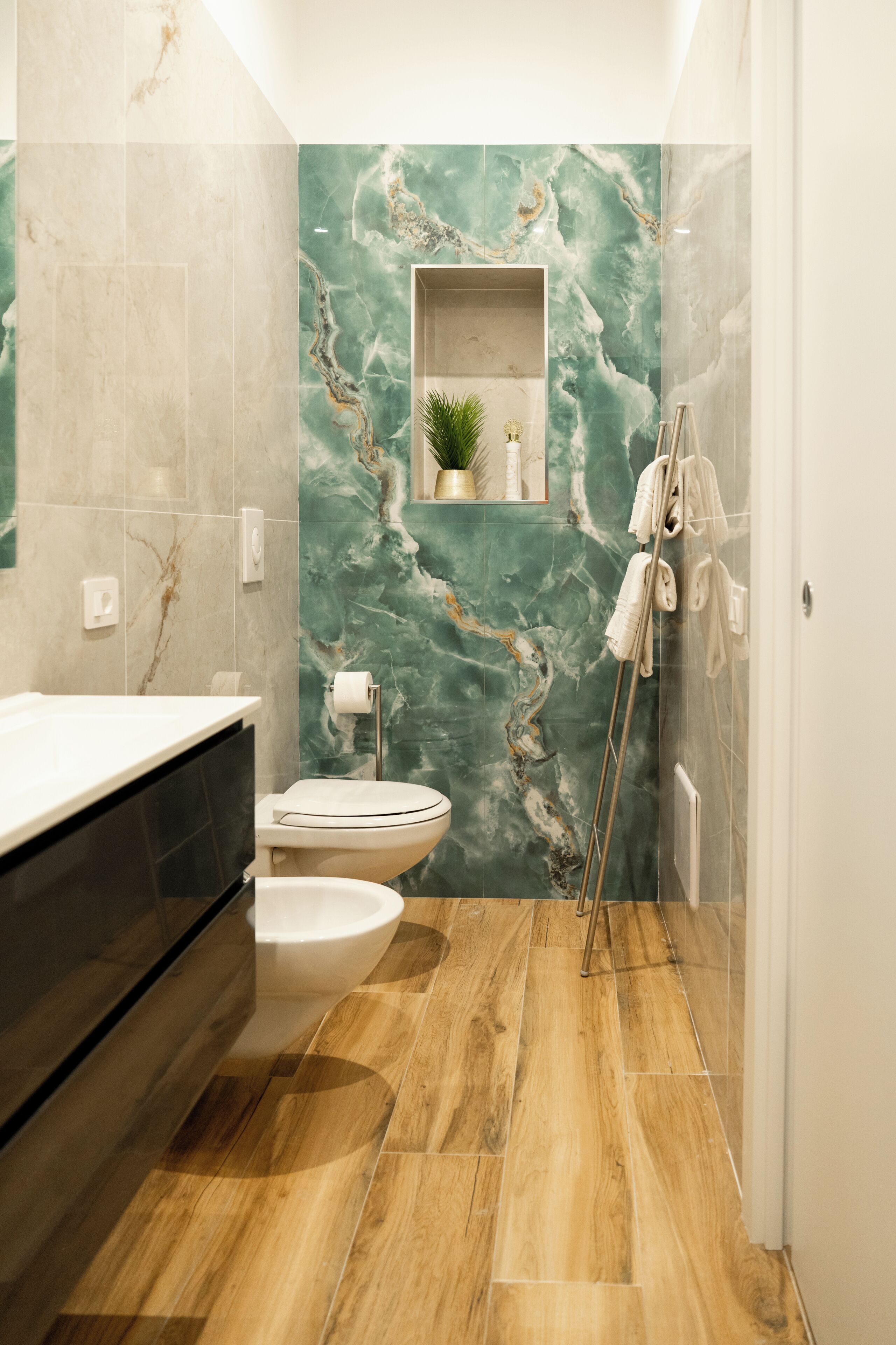 Un bagno con una parete in marmo, un pavimento in legno, un water, un lavandino e un portasciugamani.