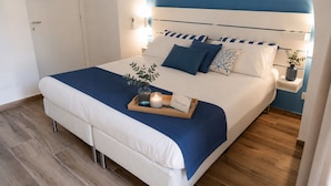 A neatly made bed with a blue and white color scheme, a bedside table with a vase and a candle, and a framed picture on the wall. - Harmonia Rooms (Civitavecchia)
