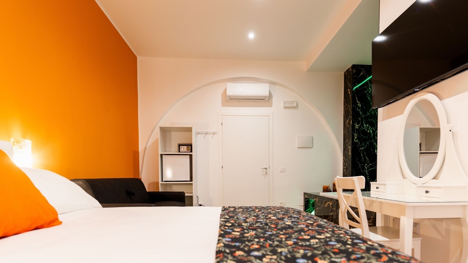 Habitació d'hotel amb llit, escriptori, cadira, mirall, una porta apuntada i aire condicionat fixat a la paret.