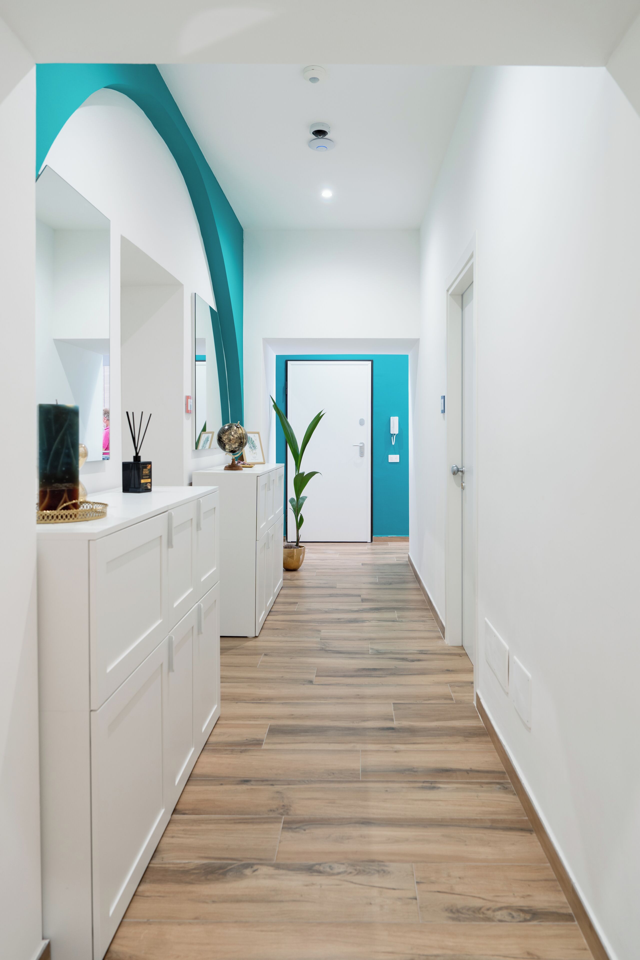 A hallway with white cabinets, a teal accent wall, a wooden floor, and a door with a teal frame.