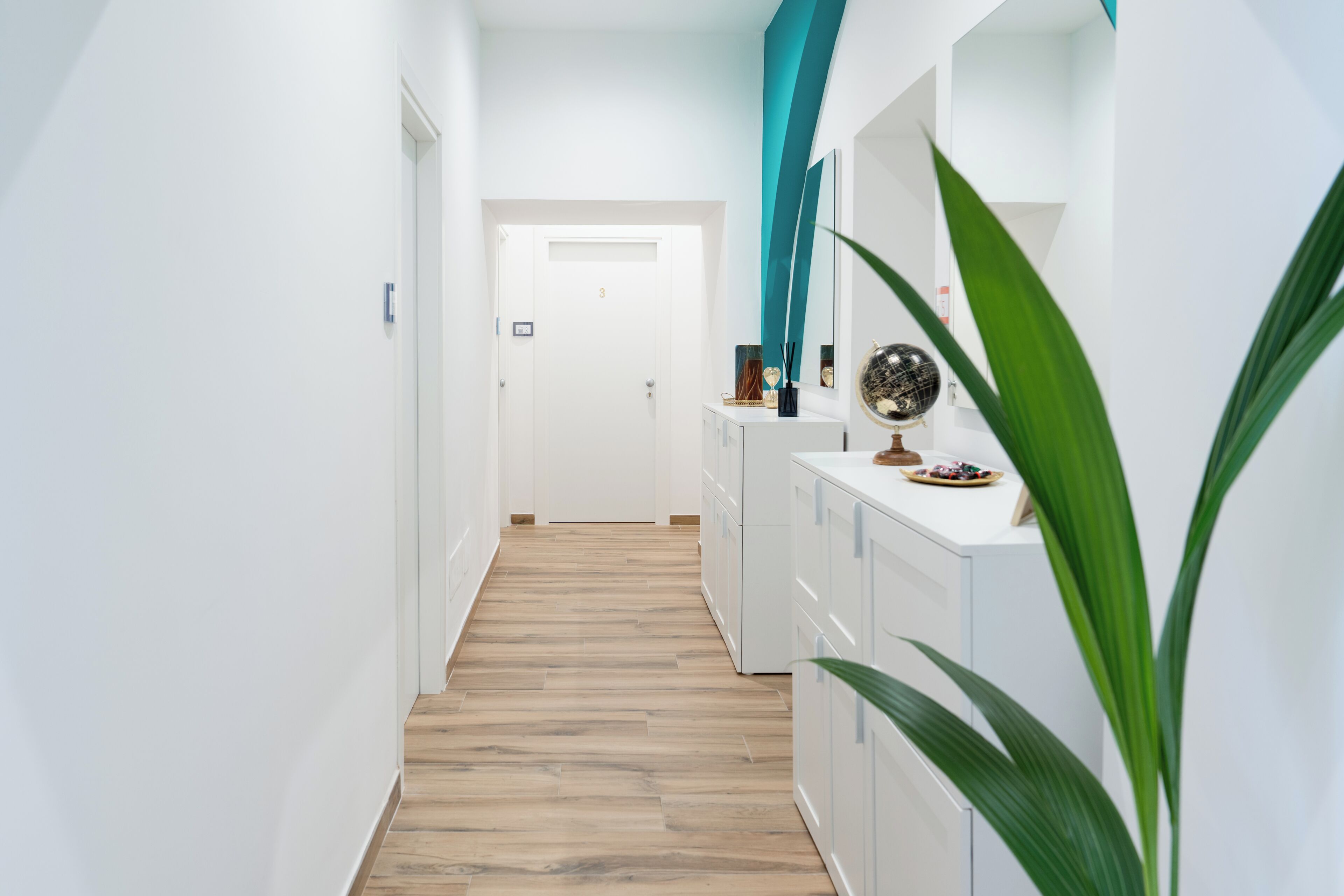 A hallway with a wooden floor, white walls, and a door at the end.