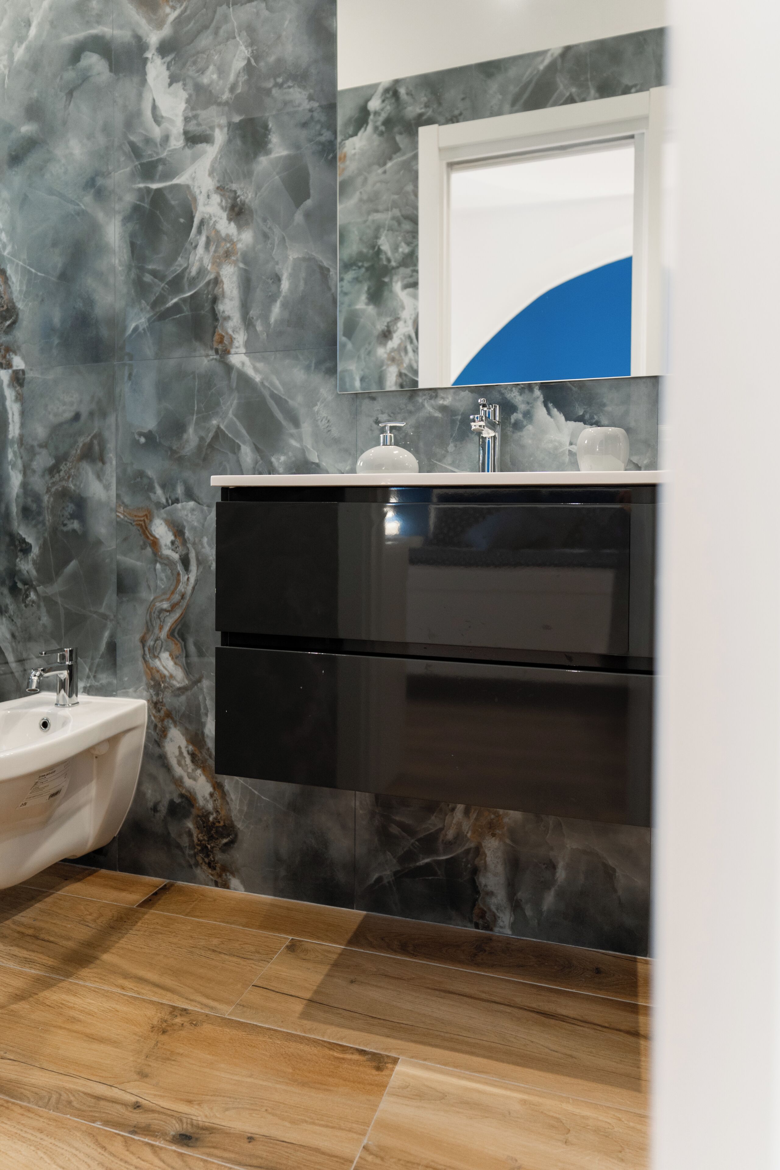 A bathroom with a marble wall, a sink, a mirror, and a black cabinet.