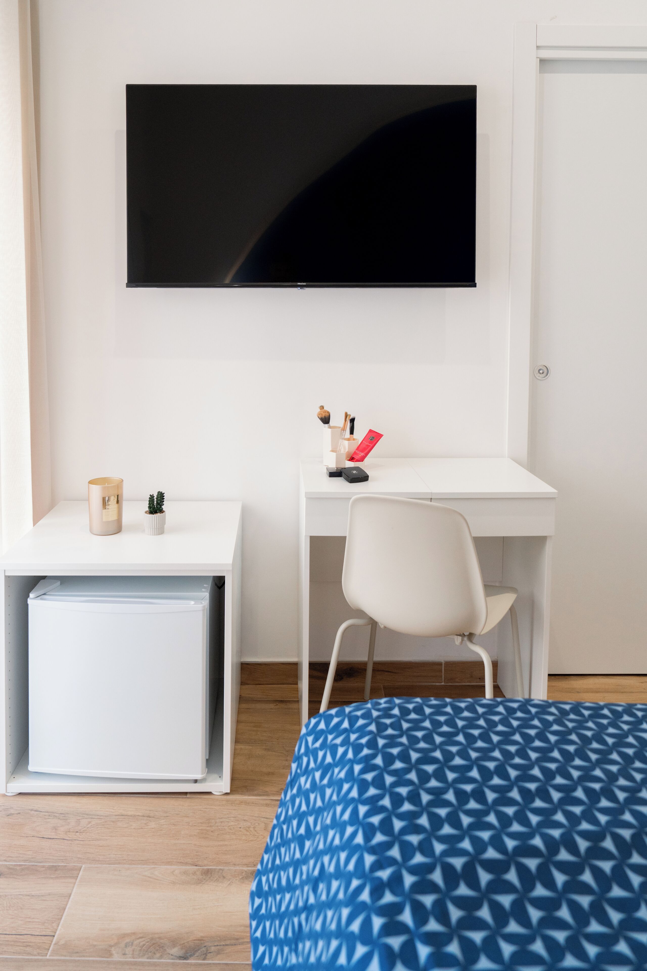 Ein Zimmer mit einem Bett, einem Schreibtisch mit Stuhl, einem an der Wand befestigten Fernseher und einem kleinen Kühlschrank.