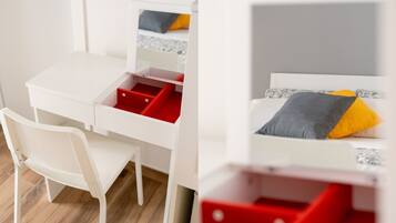 A white room with a desk, chair, and a bed with pillows.