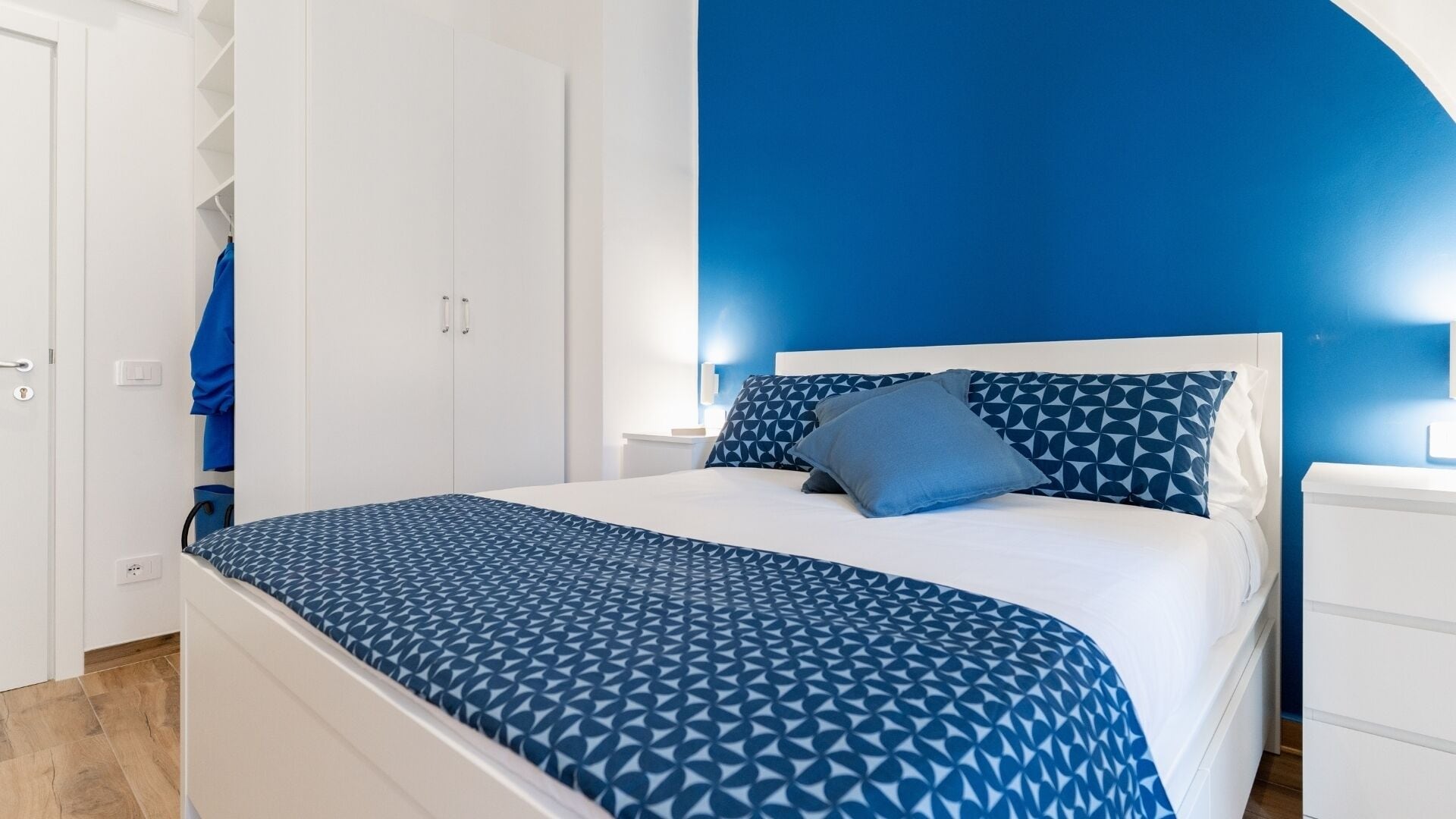 Quarto com cama, mesa de cabeceira, guarda-roupa e parede azul.