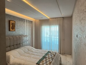 A bedroom with a bed, a headboard, a framed picture, and a window with curtains. - Quiet, central apartment ideal for families (Fès)
