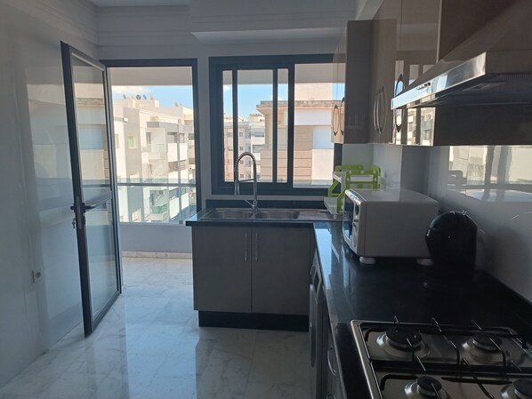 A modern kitchen with a gas stove, a sink, and a window overlooking a residential area. - Quiet, central apartment ideal for families (Fès)