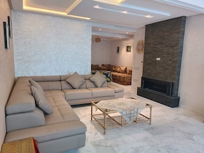 A modern living room with a sectional sofa, a fireplace, and a dining area with a table and chairs. - Quiet, central apartment ideal for families (Fès)