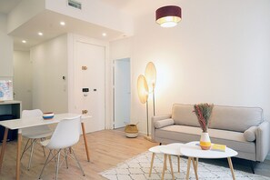 Una sala moderna con un sofá, una mesa de comedor con sillas, una mesa de centro, una lámpara de pie y una puerta que da a otra habitación.