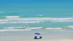 Ein Strand mit klarem Himmel, Wellen und einem blauen Sonnenschirm.