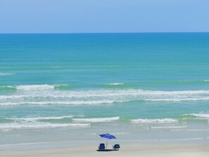 Ein Strand mit klarem Himmel, Wellen und einem blauen Sonnenschirm.
