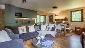 Un salon moderne avec un canapé d’angle, une table basse ronde et un coin repas comprenant une table et des chaises blanches.