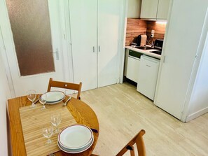 Ein Essbereich mit einem Holztisch, gedeckt für vier Personen, eine Küche mit weißen Schränken und eine Tür mit Milchglasverkleidung.