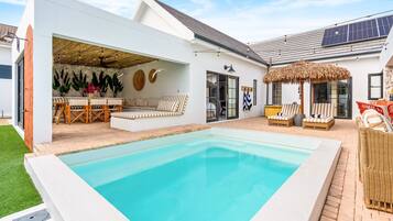 Une maison moderne dotée d’une piscine, d’un espace salon extérieur et d’un patio couvert.