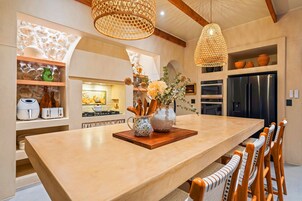 Una cocina amplia con una isla grande, electrodomésticos modernos y detalles decorativos como una lámpara de fibra y macetas de cerámica.