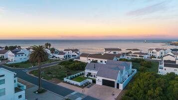 A coastal residential area with houses, a palm tree, and a view of the sea at sunset.