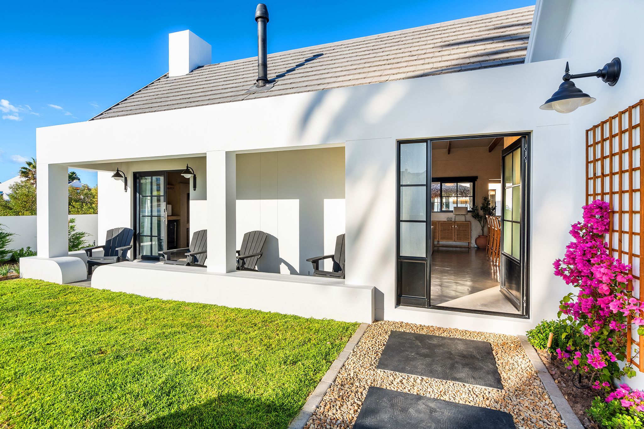 A modern house with a covered patio, outdoor seating, and a well-maintained lawn.