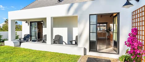 A modern house with a covered patio, outdoor seating, and a well-maintained lawn.