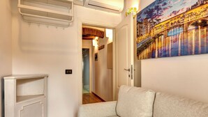 A hallway with a white wall, a white sofa, a painting of a bridge, and a door leading to another room. - Romana Apartment by Mamo Florence (Florence)