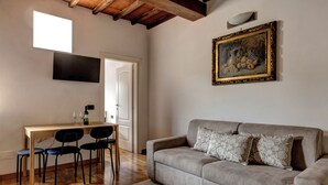 A living room with a sofa, a dining table with chairs, a TV mounted on the wall, and a painting. - Romana Apartment by Mamo Florence (Florence)