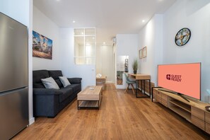 Ein modernes Wohnzimmer mit einer Couch, einem Couchtisch, einem Fernseher und einer Küche im Hintergrund.