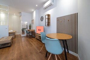 Ein modernes Zimmer mit einem Holzespeisetisch, blauen Stühlen, einer kleinen Küchenzeile und einer Wandklimaanlage.